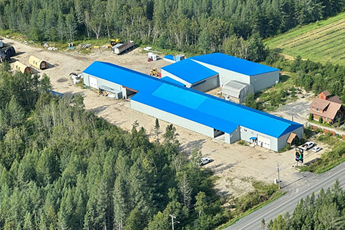 Vue aérienne de l’usine d’OSBLOCK entourée de forêt, avec les toits bleus distinctifs des bâtiments.
